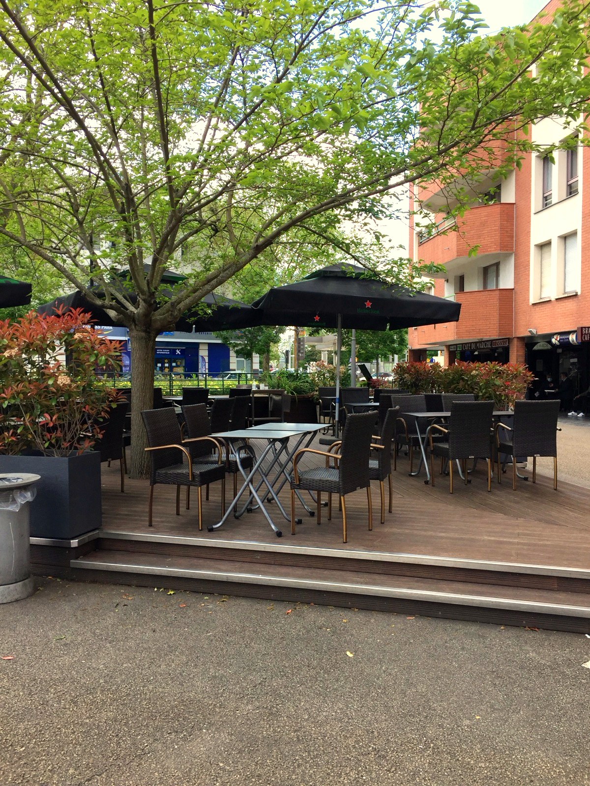 Terrasse du Café du Marché place Étienne Marcel, parasol et chaises en rotin devant l'immeuble en brique